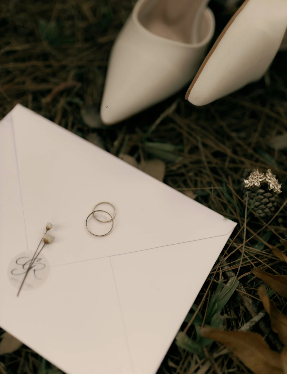 Wedding rings on an envelope beside the bride's shoes in the forest