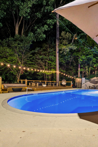 Pool lit up at night under string lights and a shade sail