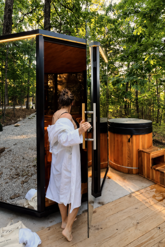 Guest in a robe stepping out of the outdoor glass sauna beside the cold plunge