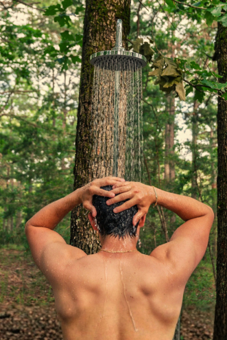 Guest rinsing off under an outdoor rain shower among the trees